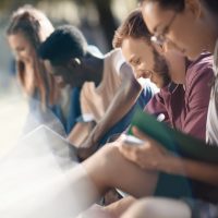 selective focus of happy multicultural students studying with books in park