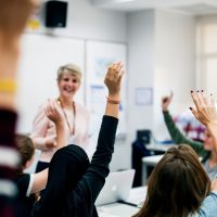 Students with their hands up responding to their teacher|Students with their hands up responding to their teacher